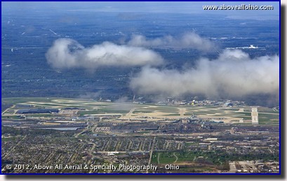 A distant oblique aerial view of Cleveland Hopkins International Airport under some fair weather cumulus clouds as viewed from above Independence, OH